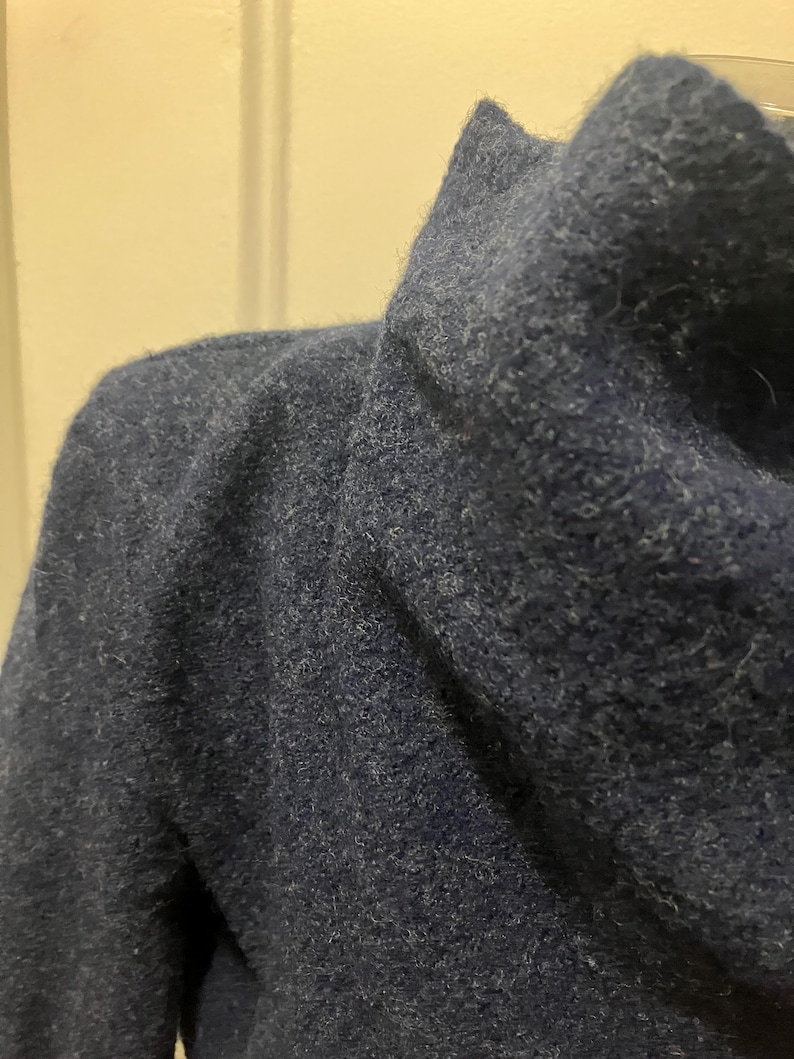 Puede incluir: Primer plano de un su&eacute;ter azul marino con cuello de cisne. El su&eacute;ter tiene una apariencia texturizada y afelpada. La tela es de color azul oscuro liso.