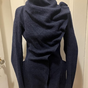 Puede incluir: Una chaqueta de lana azul marino con un cuello drapeado &uacute;nico y mangas largas. La chaqueta tiene un corte entallado y un cierre de bot&oacute;n. La tela parece ser una lana suave y texturizada.