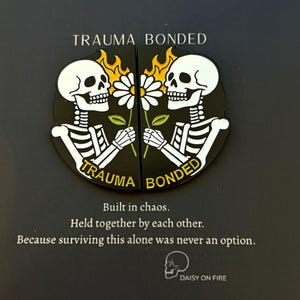 Puede incluir: Gráfico en blanco y negro con dos esqueletos sosteniendo una margarita, con llamas arriba. El texto dice "TRAUMA BONDED" y "Construido en el caos. Unidos por los demás."
