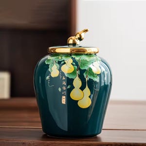 Peut inclure: Un pot en céramique vert d'eau avec un couvercle et un bouton dorés. Le pot est décoré de courges jaunes et de feuilles vertes. Le pot porte des caractères chinois.