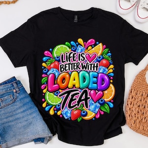 May include: A black short-sleeve t-shirt featuring a colorful graphic print that reads "LIFE IS BETTER WITH LOADED TEA" in bold, multi-colored letters, surrounded by illustrations of strawberries, blueberries, lime slices, orange slices, and ice cubes.