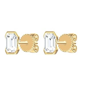 May include: A pair of stud earrings featuring emerald-cut clear stones set in yellow gold. Each earring has a rectangular stone held by a gold bezel setting and includes a matching gold post back with a textured, circular edge for secure fastening.