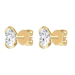 May include: A pair of stud earrings featuring oval-cut clear stones set in yellow gold bezels. Each earring includes a matching yellow gold post and a circular screw-back mechanism with a textured edge, providing a secure fit for the wearer.