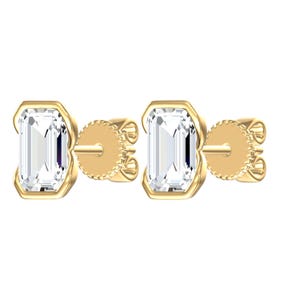 May include: A pair of stud earrings featuring emerald-cut clear stones set in yellow gold. Each earring has a rectangular stone held by a gold bezel setting, connected to a gold post and a circular, textured screw-back mechanism for secure fastening.