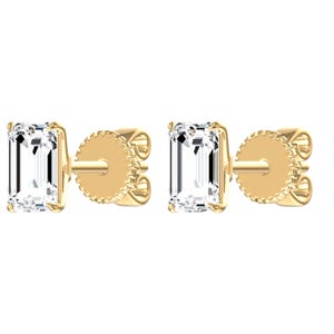 May include: A pair of stud earrings featuring emerald-cut clear stones set in yellow gold. Each earring has a rectangular faceted gemstone held by four prongs, connected to a post with a circular, textured yellow gold backing mechanism.