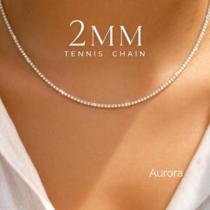 May include: A delicate 2MM tennis chain necklace with sparkling stones. The necklace is displayed on a person's neck, with the text "2MM TENNIS CHAIN" and the brand name "Aurora" in the image.