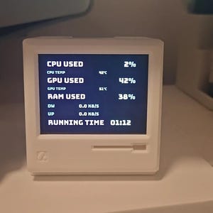 May include: A white, square-shaped computer hardware monitor with a screen displaying system statistics including CPU usage at 2%, CPU temperature at 42°C, GPU usage at 42%, GPU temperature at 51°C, RAM usage at 38%, network speeds, and running time.