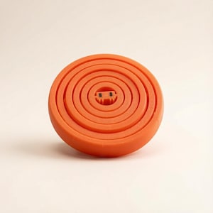 May include: A bright orange circular object featuring a series of concentric rings that create a stepped, bowl-like structure. At the very center of the object, there is a small, rectangular orange component with two tiny black square markings.