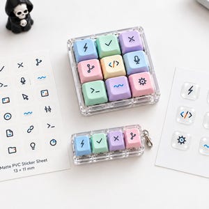 May include: A clear acrylic 3x3 macro keypad and a 1x4 keychain keypad with pastel-colored keycaps featuring various icons. Includes a matte PVC sticker sheet with 13 x 11 mm icons and a small sheet of six clear, raised, square-shaped stickers.