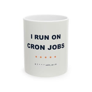 Peut inclure: Un mug en céramique blanche avec le texte bleu foncé I RUN ON CRON JOBS, suivi de cinq astérisques orange et du petit texte noir 0 7 * * * wake_up.sh imprimé sur la surface avant du récipient cylindrique.
