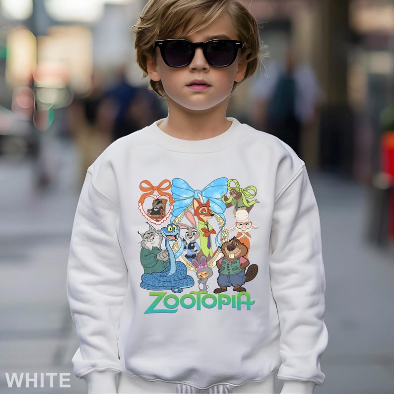 May include: White sweatshirt featuring a colorful graphic of characters from the animated movie "Zootopia". The design includes a blue bow, various animal characters, and the word "Zootopia" in green. The sweatshirt is worn by a person wearing sunglasses.