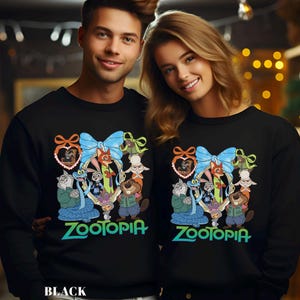 May include: Black sweatshirts featuring a colorful Zootopia design. The design includes various cartoon characters, a blue bow, and the word "Zootopia" in green. The sweatshirts are worn by two people.