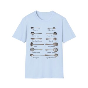 May include: Pale blue t-shirt with a graphic of different types of spoons, each labelled. The design includes a teaspoon, tablespoon, ladle, and others. Text includes "Teaspoon", "Tablespoon", "Ladle", "Coffee Spoon", "Soup Spoon", and more.