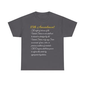 Puede incluir: Camiseta gris oscuro con el texto de la 15ª Enmienda de la Constitución de los Estados Unidos. El texto está en oro y blanco, con el título de la enmienda en oro. La camiseta es de cuello redondo y está hecha de un material suave.