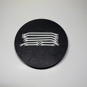 May include: A collection of white, curved, plastic rods with small holes at each end, arranged on a black circular surface. The rods have a smooth, clean appearance and are evenly spaced.