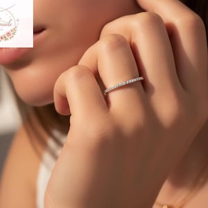 May include: A silver ring set with small, sparkling stones. The ring is on a person's finger, with the hand in focus. The ring is a delicate piece of jewellery, suitable for everyday wear or special occasions.