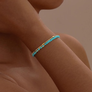 May include: A double-strand bracelet featuring one row of small, round, bright turquoise beads and one row of thin gold-toned metal chain. The two strands are connected, creating a layered look with alternating gold-toned beads and turquoise beads.