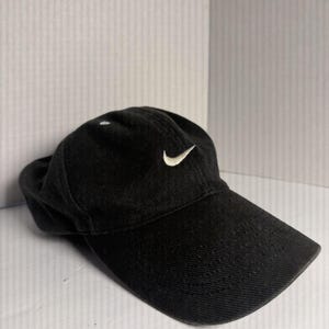 May include: Black baseball cap with a curved brim. The cap features a white Nike swoosh logo on the front. The hat is made of a textured fabric.