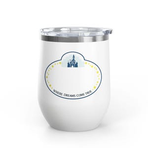 Peut inclure: Gobelet à vin isotherme blanc avec couvercle transparent. Le gobelet présente un motif bleu et jaune avec un château et le texte "WHERE DREAMS COME TRUE". Le motif est de forme ovale avec des étoiles.