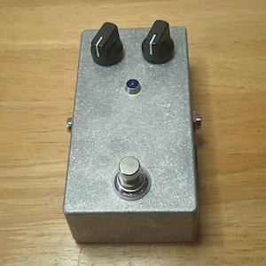 May include: A rectangular guitar effects pedal with a brushed silver metal enclosure. The device features two black control knobs with white indicator lines, a single blue LED indicator light, and one silver metal footswitch on the front.