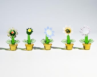 Puede incluir: Cinco esculturas de flores de cristal de colores en macetas amarillas. Cada flor tiene un diseño diferente, con tallos y hojas verdes. Las flores son en tonos de amarillo, verde, azul y blanco, creando una exhibición alegre.