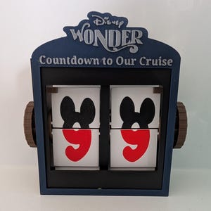 Könnte beinhalten: Ein Disney Wonder Countdown-Kalender in Marineblau. Oben am Rahmen befindet sich das Disney Wonder-Logo. Der Kalender zeigt die Zahl 99 mit Mickey Mouse-Ohren. Der Text "Countdown to Our Cruise" steht unter dem Logo.