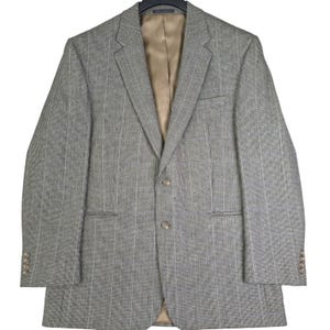 May include: A grey blazer featuring a subtle vertical pinstripe pattern, a notched lapel, and two front buttons. The garment includes a tan interior lining, a single chest pocket, two side flap pockets, and four small buttons on each sleeve cuff.