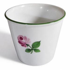 May include: A white ceramic cup with a tapered shape and a thin green rim. The exterior features a hand-painted illustration of a single pink rose with green leaves and a stem. The interior of the cup is plain white and smooth in texture.