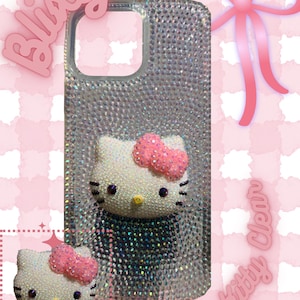 May include: A clear phone case covered in small, sparkling rhinestones. The case features a 3D Hello Kitty design with a pink bow. The background is pink with the words "Blixity" and "Hello Kitty Clear" in pink.