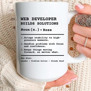 Könnte beinhalten: Weiße Keramik-Tasse mit dem Text "WEB DEVELOPER BUILDS SOLUTIONS" in Schwarz. Die Tasse enthält eine Definition eines Webentwicklers mit Aufzählungszeichen, die seine Fähigkeiten und Eigenschaften beschreiben. Die Tasse wird von einer Person gehalten.
