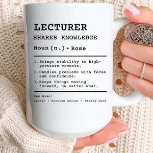 Puede incluir: Taza de cerámica blanca con el texto "LECTURER SHARES KNOWLEDGE" en negro. La taza incluye una definición de un profesor, con viñetas que describen sus cualidades. La taza está sostenida por una persona.
