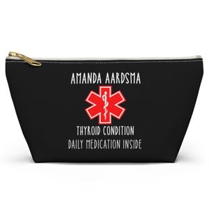 May include: Black zippered pouch with the text "AMANDA AARDSMA" above a red medical symbol and the words "THYROID CONDITION DAILY MEDICATION INSIDE". The pouch has a gold zipper.
