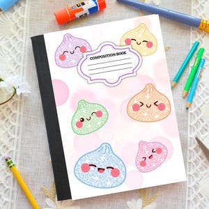 May include: A composition book with a white cover featuring a pattern of colorful, glittery, smiling dumpling characters. A central white label with a purple border contains the text COMPOSITION BOOK with four horizontal lines for writing.