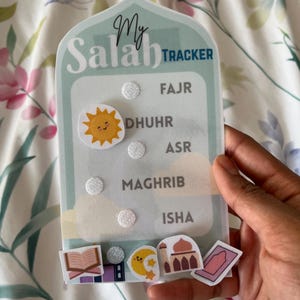 May include: A light blue "My Salah Tracker" with a sun and cloud stickers. The tracker has spaces for Fajr, Dhuhr, Asr, Maghrib, and Isha. Additional stickers include a book, crescent moon, mosque, and prayer rug.