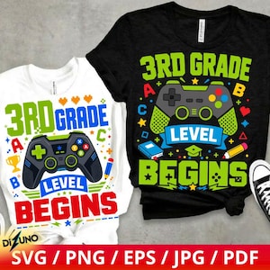 May include: A white t-shirt and a black t-shirt, both featuring a graphic of a video game controller, the text 3RD GRADE LEVEL BEGINS, and colorful icons including a trophy, pencil, book, and letters, arranged in a vibrant, multi-colored design.