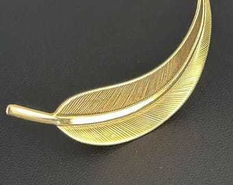 Broche vintage de pluma curva en tono dorado con textura de hoja y penacho.