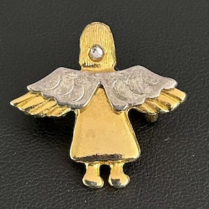 May include: A gold-tone metal angel brooch featuring a textured head with a single clear rhinestone accent. The figure has silver-tone wings with etched feather details and a smooth gold-tone body and feet, creating a two-tone metallic design.