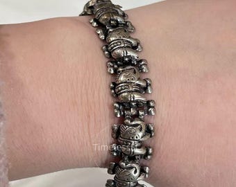 May include: Silver-toned bracelet featuring a repeating design of stylized figures. Each figure is intricately detailed, with visible facial features and body ornamentation. The bracelet is worn on a wrist, showcasing its design and craftsmanship.