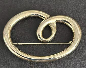 Broche abstracto vintage en tono dorado, estilo modernista, con lazo abierto.