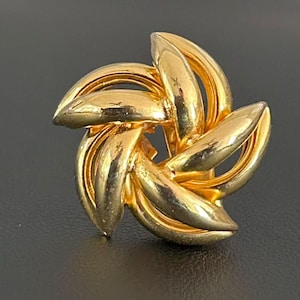 May include: A gold-toned metal earring featuring a swirling, multi-layered star or flower-like design. The piece is composed of several smooth, curved, and overlapping segments that create a dimensional, circular shape with a polished, reflective finish.