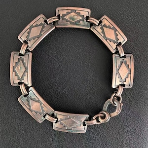 May include: A vintage copper bracelet with rectangular links, each featuring a diamond and geometric pattern. The bracelet has a tarnished patina, and a clasp with the word "COPPER" is visible.