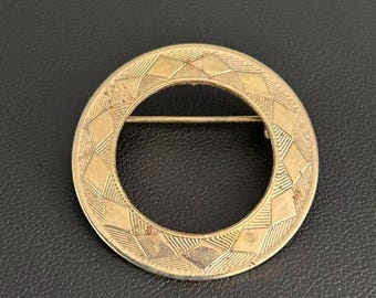 Broche vintage de círculo geométrico en tono dorado con patrón de diamante grabado.
