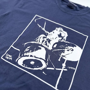 May include: Navy blue t-shirt featuring a white graphic of a drummer playing a drum set. The image is inside a white square. The text "LEVON HELM" is in the lower left corner. The shirt is made of a soft material.