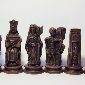 Può includere: Un set di pezzi degli scacchi intagliati in modo intricato in un colore marrone scuro. I pezzi raffigurano figure con abiti e accessori dettagliati, tra cui un re, una regina e altre figure degli scacchi. Il set di scacchi è esposto su uno sfondo bianco.