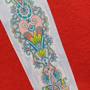 May include: A colorful, hand-drawn bookmark with an intricate floral and geometric design. The bookmark features a light blue background with a central design in pink, teal, yellow, and blue. The design includes flowers, swirls, and geometric shapes.