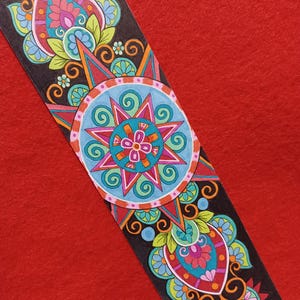 May include: A colorful, hand-drawn bookmark with a black background and intricate floral and geometric designs. The bookmark features a central circular design with teal, pink, and orange accents, and is set against a red background.