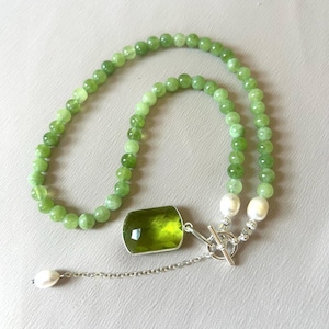 May include: A necklace featuring a strand of round light green beads, a large rectangular faceted lime green pendant, two white oval pearls, and a silver-toned toggle clasp with a short chain extension ending in a single white pearl.