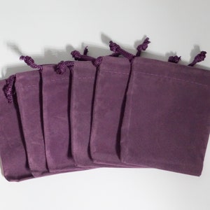 May include: Six purple velvet drawstring pouches with a gathered top. The pouches are arranged in a row with the openings facing the viewer.