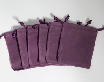 May include: Six purple velvet drawstring pouches with a gathered top. The pouches are arranged in a row with the openings facing the viewer.