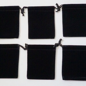 May include: Six black velvet drawstring pouches, each with a small opening at the top. The pouches are arranged in two rows of three, with the top row slightly offset from the bottom row.